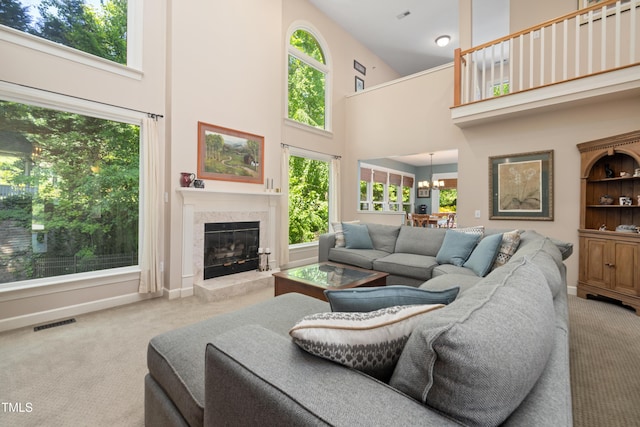 carpeted living room featuring visible vents, a healthy amount of sunlight, a high end fireplace, and a towering ceiling