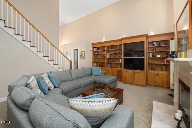 living area featuring light colored carpet, stairs, a high ceiling, and a tile fireplace