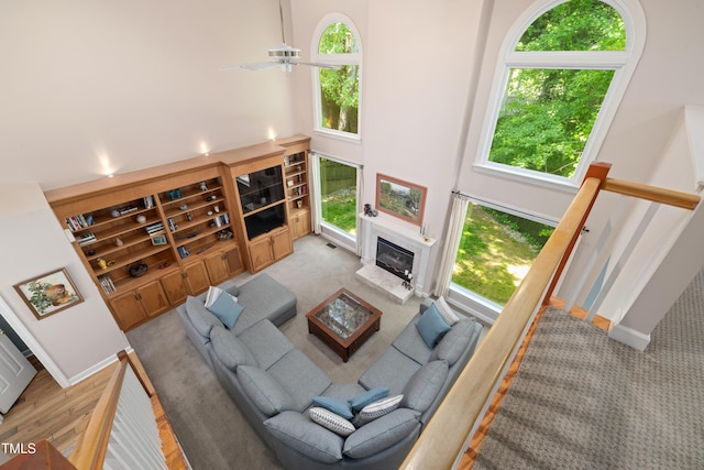 living room with carpet, a towering ceiling, a glass covered fireplace, and ceiling fan