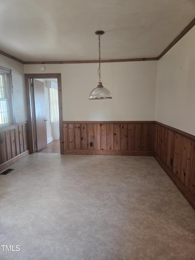 empty room with ornamental molding, a wainscoted wall, and wood walls