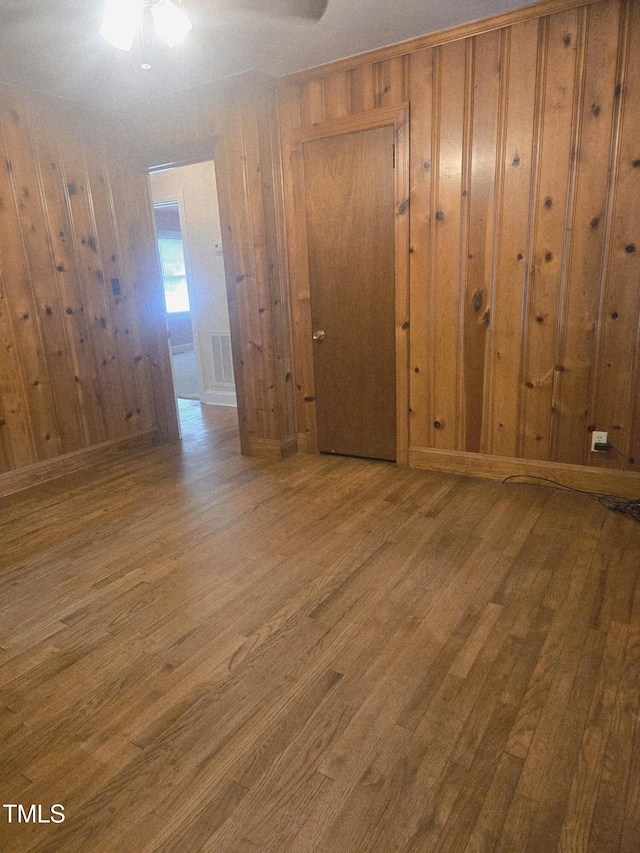 empty room featuring wood finished floors, wood walls, and a ceiling fan