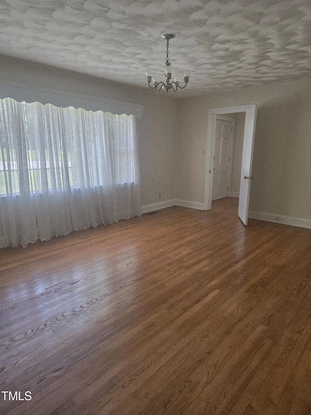 unfurnished room featuring a chandelier, baseboards, and wood finished floors