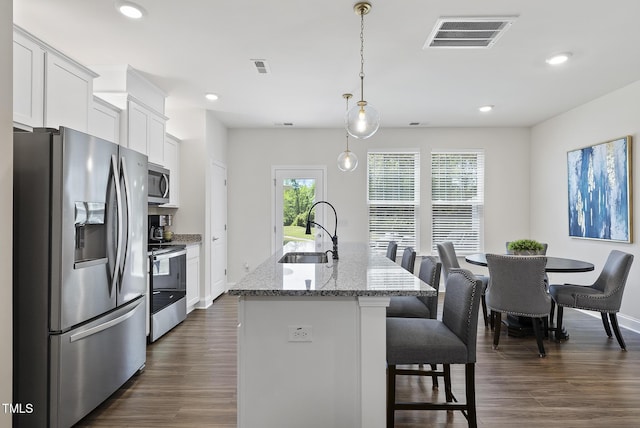 kitchen with visible vents, a kitchen island with sink, a breakfast bar, a sink, and appliances with stainless steel finishes