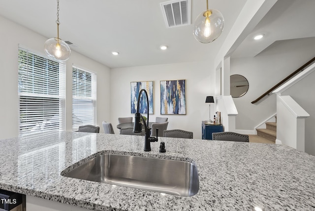 kitchen with hanging light fixtures, light stone counters, a sink, recessed lighting, and visible vents