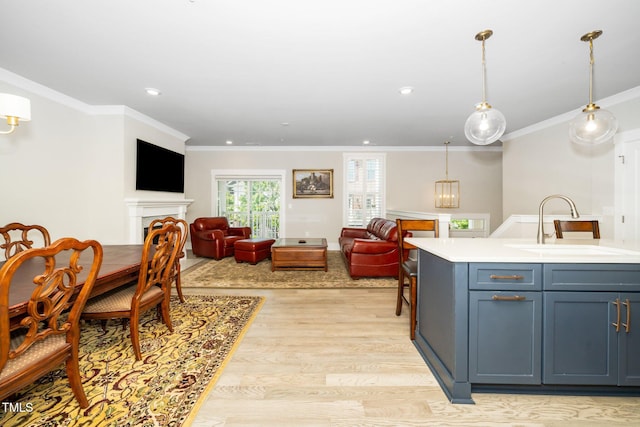 kitchen featuring crown molding, light countertops, a sink, open floor plan, and light wood-style flooring