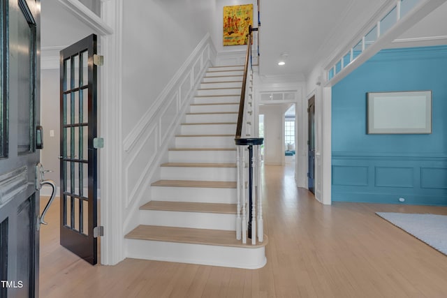 staircase with a wainscoted wall, ornamental molding, a decorative wall, and wood finished floors