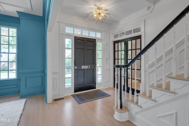 entryway with stairs, ornamental molding, wood finished floors, and a decorative wall