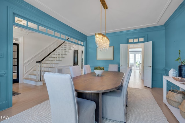 dining space with an inviting chandelier, wood finished floors, stairway, and a decorative wall