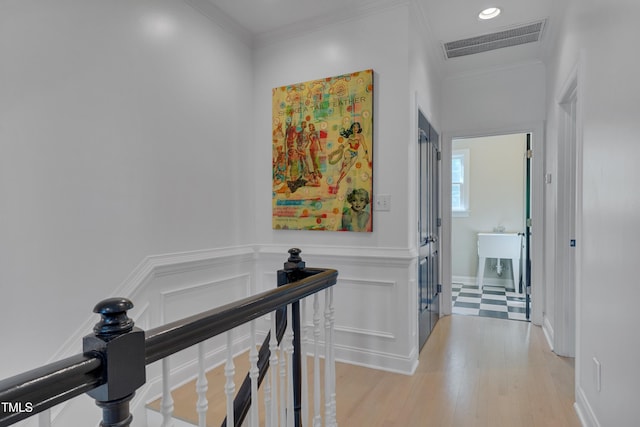 hall featuring light wood finished floors, a wainscoted wall, an upstairs landing, visible vents, and ornamental molding
