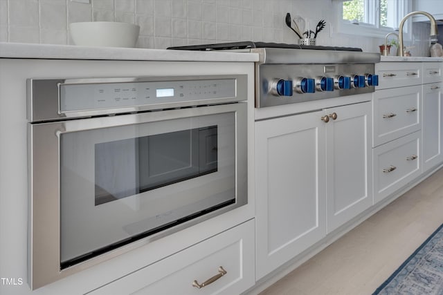 room details featuring white cabinets, appliances with stainless steel finishes, a sink, light wood-style floors, and decorative backsplash