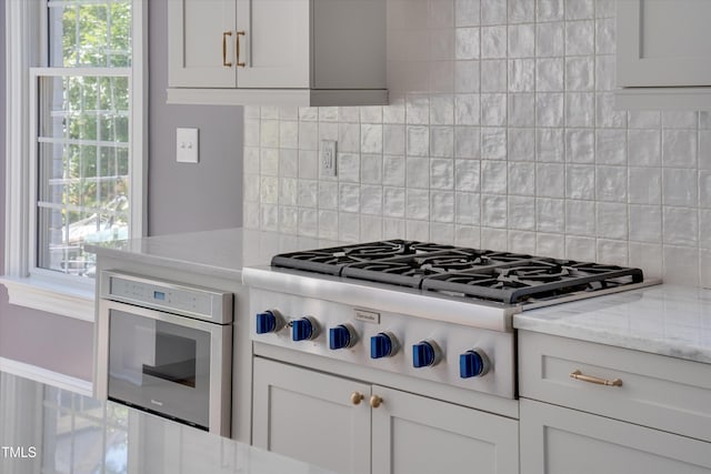 kitchen with white cabinets, tasteful backsplash, light stone countertops, and stainless steel appliances
