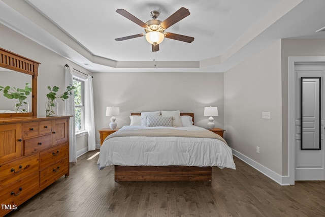 bedroom featuring visible vents, wood finished floors, baseboards, ceiling fan, and a tray ceiling