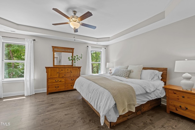 bedroom featuring baseboards, ceiling fan, a tray ceiling, and wood finished floors