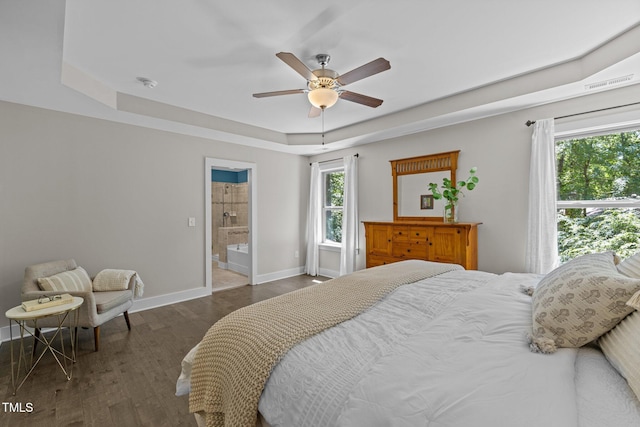 bedroom featuring a ceiling fan, wood finished floors, baseboards, a raised ceiling, and connected bathroom