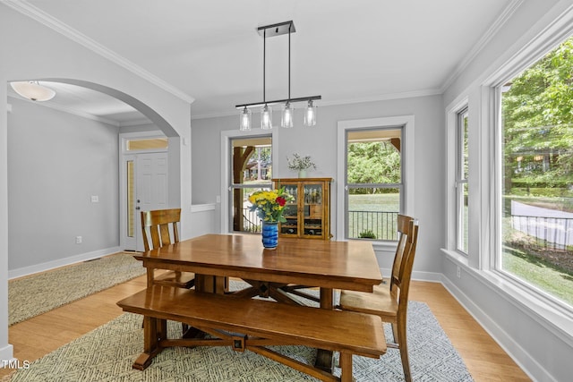 dining space featuring arched walkways, light wood finished floors, and a healthy amount of sunlight