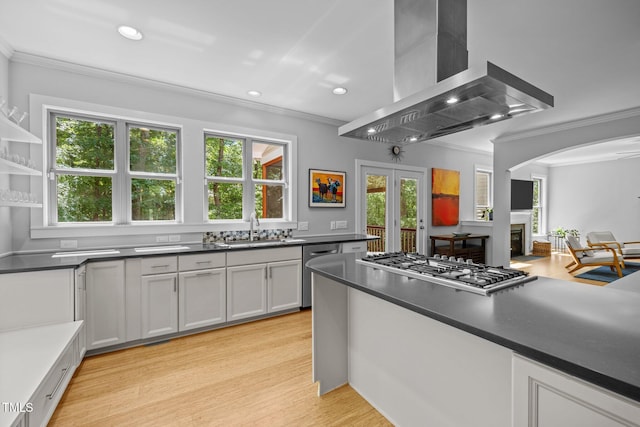 kitchen featuring ornamental molding, a glass covered fireplace, wall chimney range hood, a sink, and appliances with stainless steel finishes