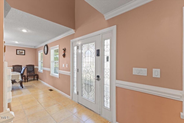 tiled foyer with a textured ceiling, visible vents, ornamental molding, and baseboards