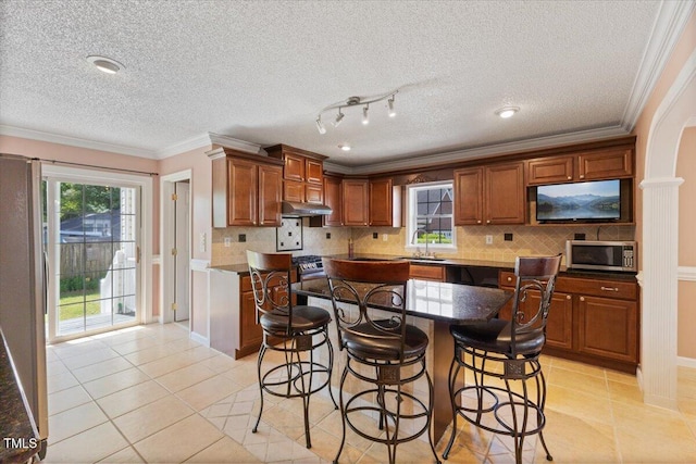 kitchen featuring decorative backsplash, ornamental molding, a kitchen bar, appliances with stainless steel finishes, and light tile patterned floors
