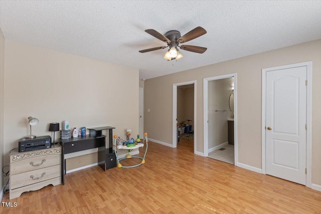 interior space featuring a textured ceiling, ceiling fan, baseboards, and light wood finished floors