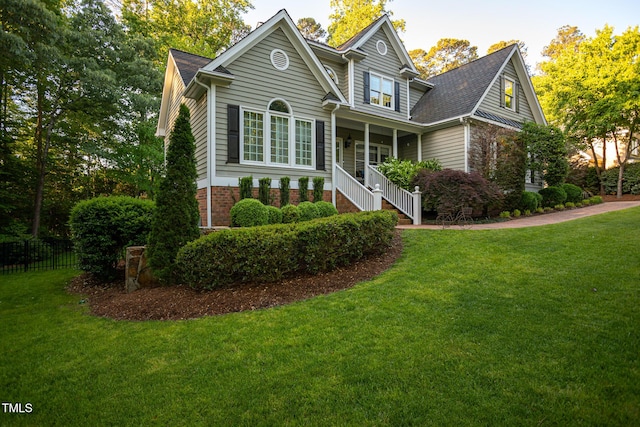 view of front of property with fence, roof with shingles, a porch, and a front lawn
