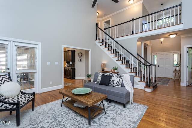 living room featuring crown molding, stairs, wood finished floors, baseboards, and a high ceiling