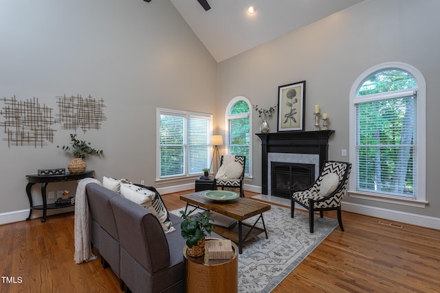 living area featuring visible vents, wood finished floors, high vaulted ceiling, baseboards, and a premium fireplace