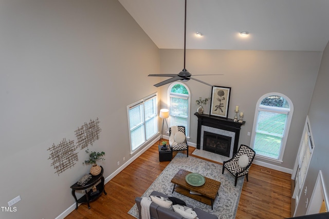 living room with a glass covered fireplace, wood finished floors, baseboards, high vaulted ceiling, and a ceiling fan