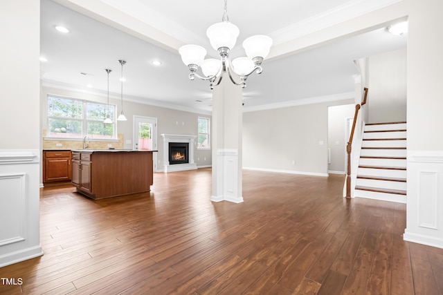 unfurnished living room with crown molding, a glass covered fireplace, dark wood-type flooring, a sink, and a notable chandelier