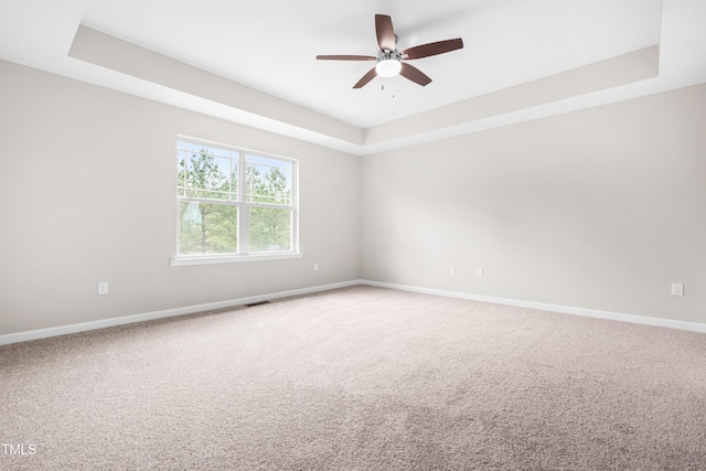 carpeted empty room with baseboards, visible vents, a ceiling fan, and a raised ceiling