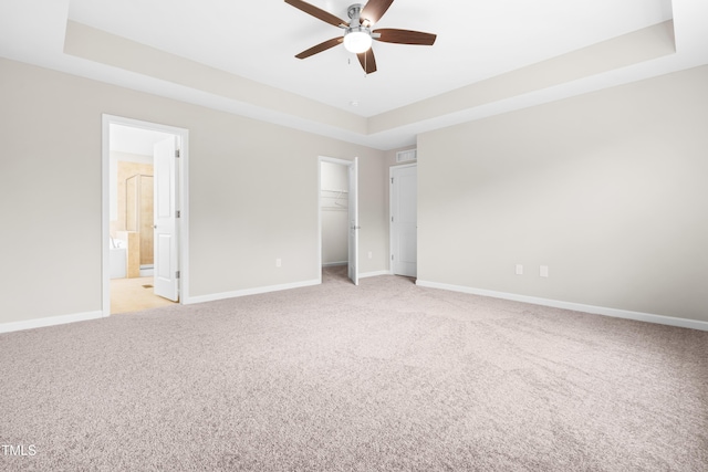unfurnished bedroom featuring baseboards, light carpet, a tray ceiling, and a spacious closet