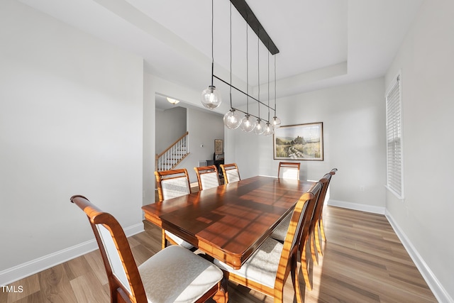 dining area featuring light wood-type flooring, baseboards, and stairway