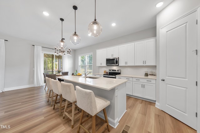 kitchen with a kitchen breakfast bar, light wood-type flooring, white cabinets, a sink, and appliances with stainless steel finishes