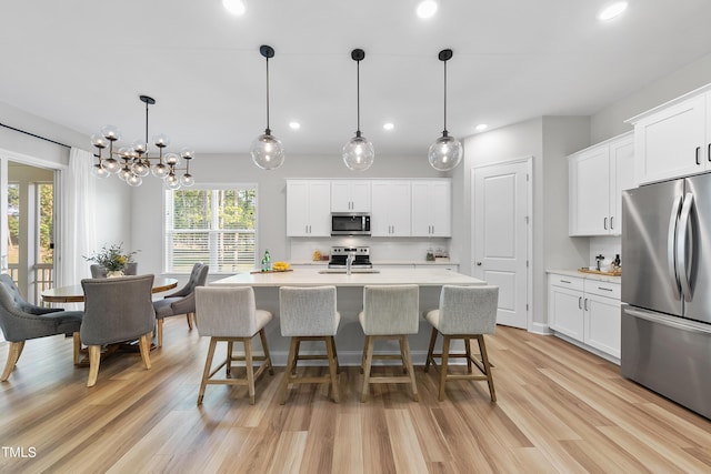 kitchen featuring a kitchen breakfast bar, a center island with sink, light countertops, light wood finished floors, and appliances with stainless steel finishes
