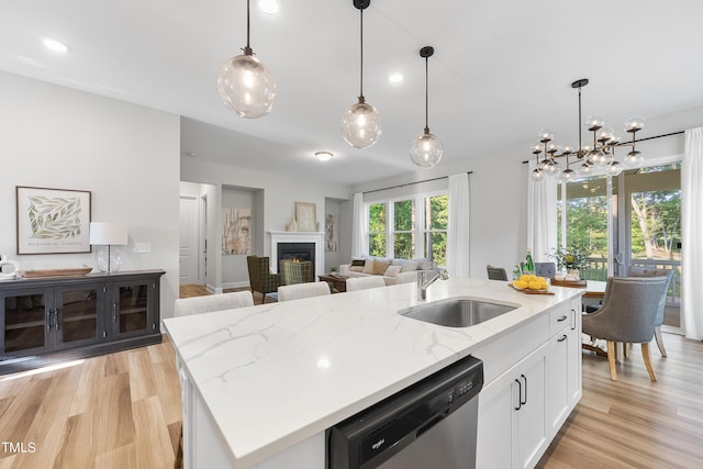 kitchen with stainless steel dishwasher, white cabinetry, a sink, light wood-style flooring, and an island with sink