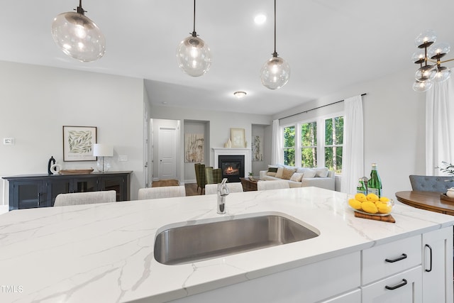 kitchen featuring open floor plan, a glass covered fireplace, decorative light fixtures, and light stone countertops