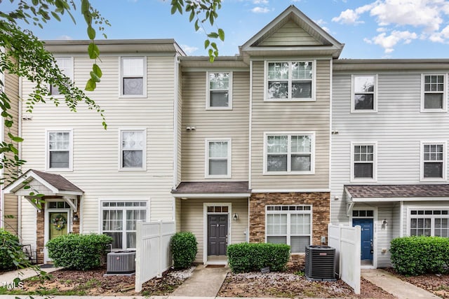 townhome / multi-family property featuring central AC unit, stone siding, and fence