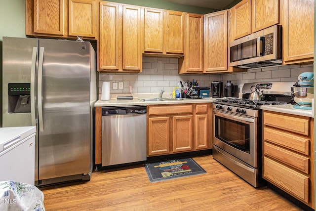 kitchen with appliances with stainless steel finishes, light countertops, decorative backsplash, light wood-style floors, and a sink