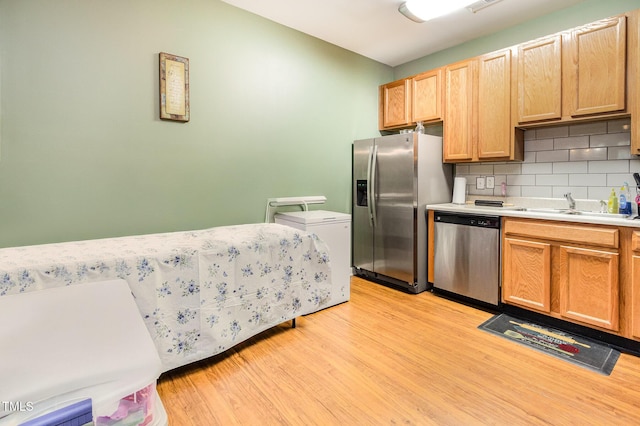 kitchen featuring appliances with stainless steel finishes, light wood-type flooring, decorative backsplash, light countertops, and a sink
