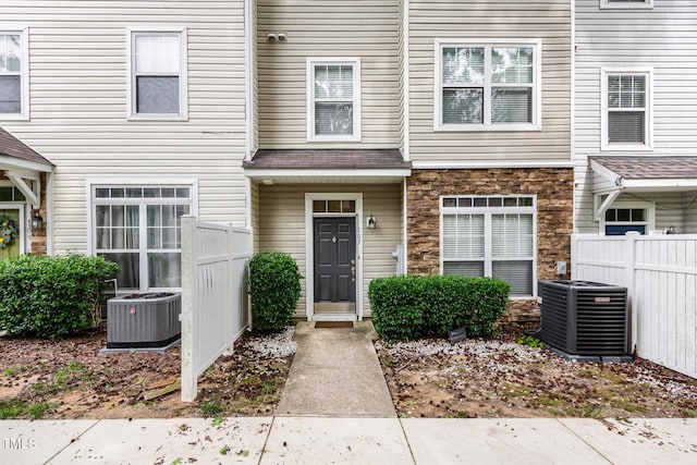 entrance to property featuring stone siding, fence, and central AC unit