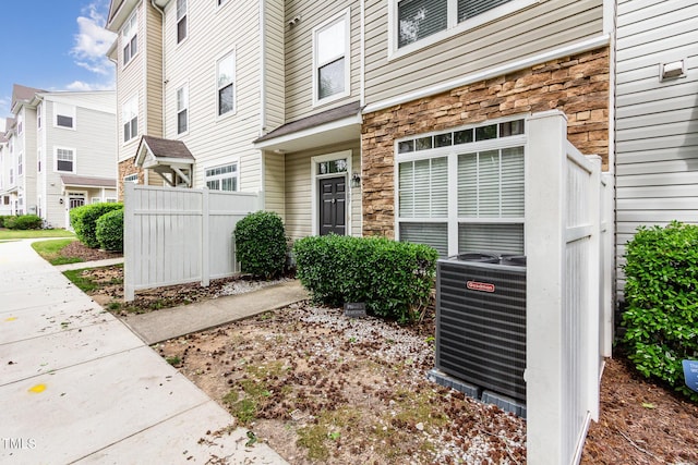 doorway to property with stone siding, central AC, fence, and a residential view