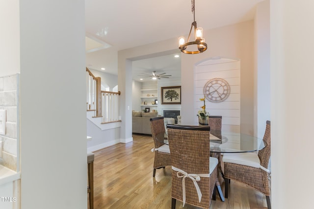 211 Page St, Morrisville, NC 27560 - dining room with light wood-style floors, a glass covered fireplace, ceiling fan with notable chandelier, baseboards, and stairway