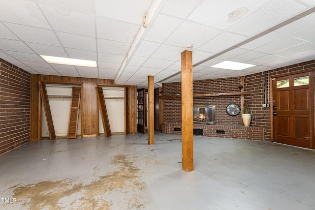 basement featuring a paneled ceiling, brick wall, and a fireplace