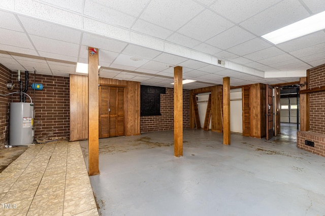 finished basement with water heater, a drop ceiling, and brick wall