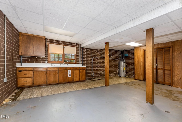 below grade area featuring a sink, water heater, a drop ceiling, and brick wall