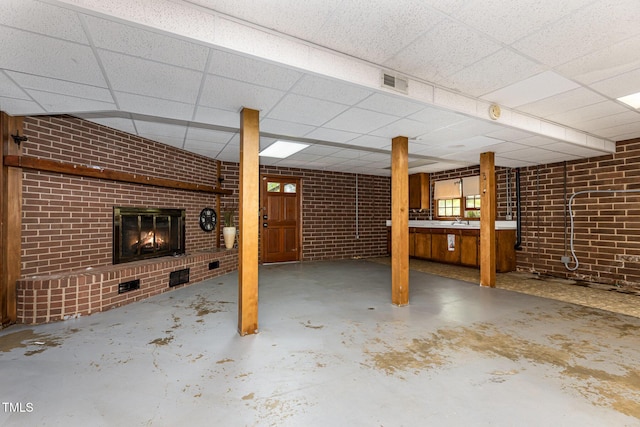 basement featuring brick wall, visible vents, a paneled ceiling, and a fireplace
