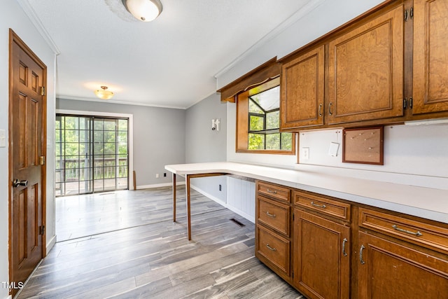 kitchen with brown cabinetry, light countertops, crown molding, and light wood-type flooring