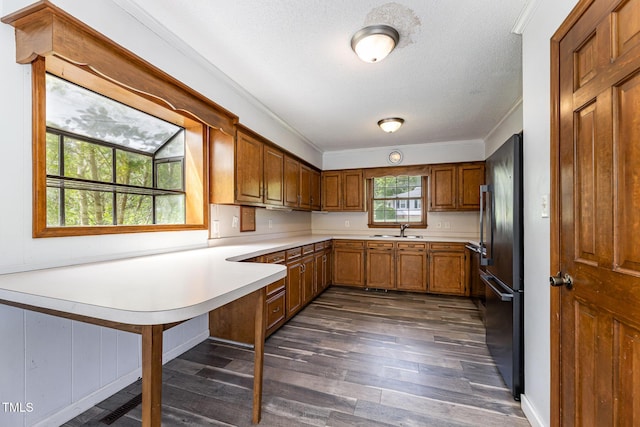 kitchen featuring brown cabinets, a sink, light countertops, freestanding refrigerator, and dark wood-style floors