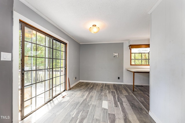 empty room featuring crown molding, a textured ceiling, baseboards, wood finished floors, and visible vents
