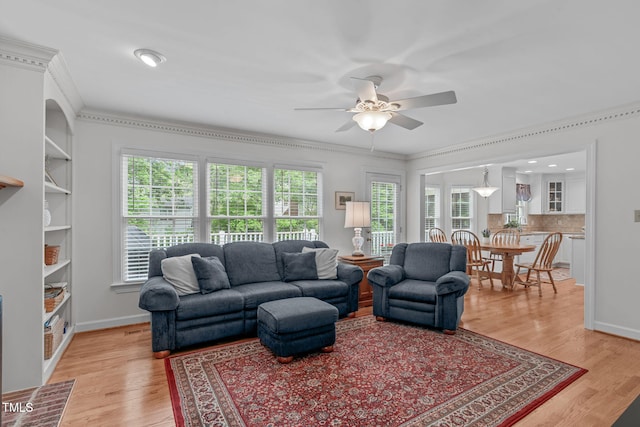 living room featuring a ceiling fan, ornamental molding, light wood-style floors, and baseboards