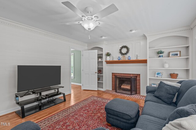 living area featuring wood finished floors, a ceiling fan, crown molding, baseboards, and a fireplace